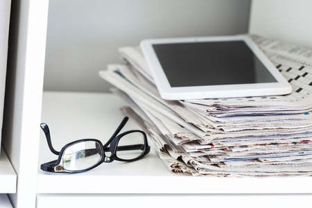 Stack of newspapers and tablet on wooden tableの写真素材