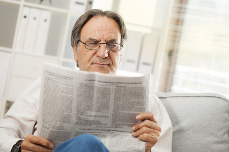 Senior man reading newspaper in homeの写真素材
