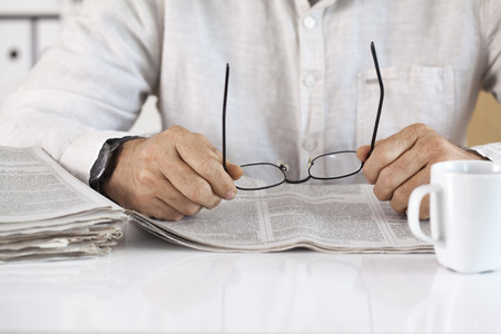 Man reading newspaper and holding eyeglassesの写真素材