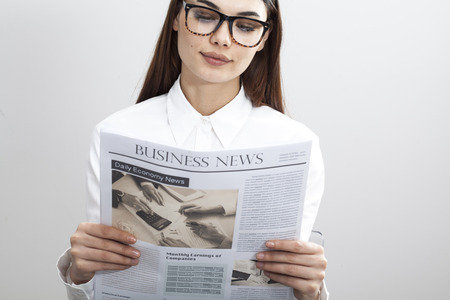 Businesswoman reading newspaper on gray backgroundの写真素材