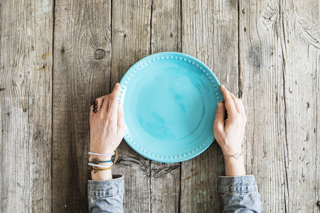 Woman hands holding blank plate on wooden tableの写真素材