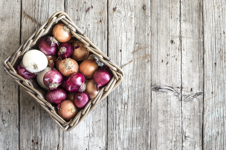 Raw onions in basket on wooden tableの写真素材