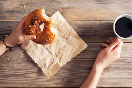 Female hands eating pastry with coffee on wooden tableの写真素材