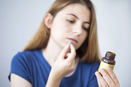 Young woman taking a pill while reading the bottleの写真素材