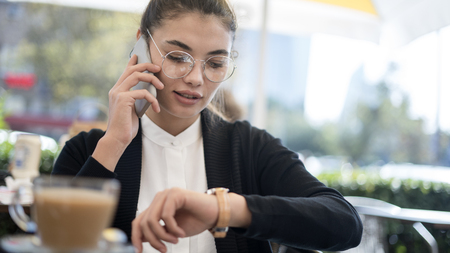 Businesswoman talking mobile phone and looking at watch in the outdoorsの写真素材