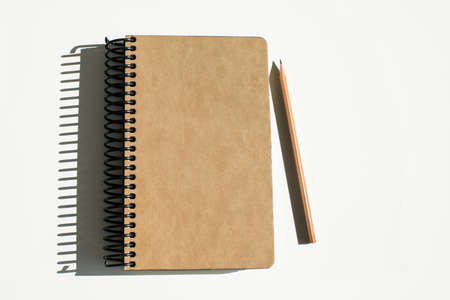 Spiral light brown notebook beside pencil on white backgroundの写真素材