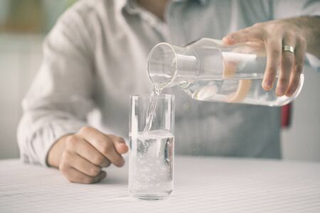 Young man pouring water from bottle to glass