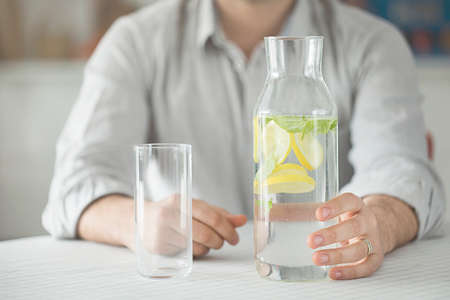 Young man having bottle of water and glass in kitchenの写真素材