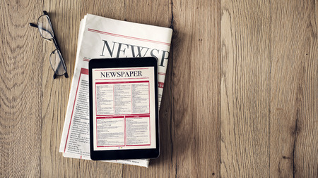 Reading news on tablet and newspaper on wooden backgroundの写真素材