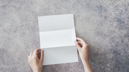 Female hands holding blank white folded paper on backgroundの写真素材