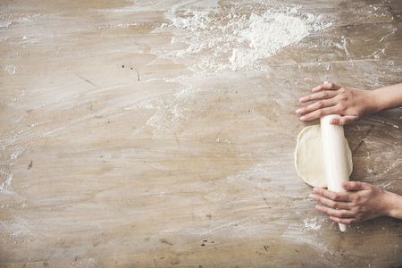 Female hands rolling dough on wooden tableの写真素材