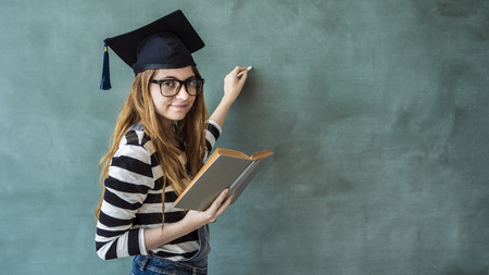 Female student writing on green chalkboardの写真素材