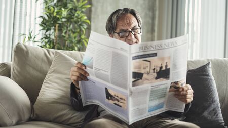Senior man reading newspaper at homeの写真素材