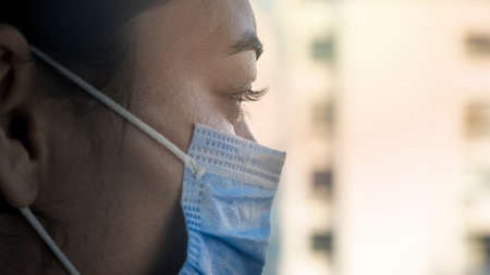 Young woman looking through the window and wearing mask protectionの写真素材