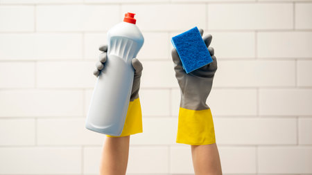 Gloved hands holding detergent and sponge raised upの写真素材