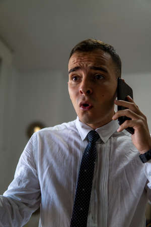 Young businessman speaks altered on the phone. He seems worried about the news he has been given. He is wearing a shirt and tie.の写真素材