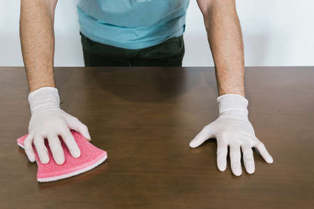 Unrecognizable man cleaning a table with gloves and a sponge. He is carrying a spray of cleaning liquid.の写真素材
