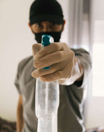 Man pointing disinfectant spray at camera. He is wearing an anti-contamination mask because of the covid-19. Focus on the spray.の写真素材