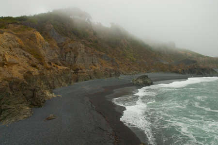 Foggy cliffside overlooks black sand beachの写真素材