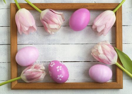 Easter composition. Easter eggs, photo frame, tulips on a white wooden background. Flat layout, top...