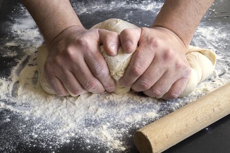 men's hands knead dough on a floured table.の写真素材