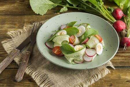spring vitamin salad with fresh vegetables on a wooden table.の写真素材