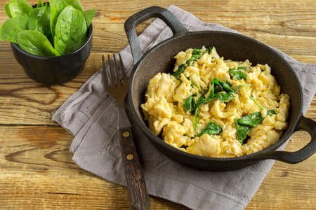scrambled eggs with spinach and tomatoes on a white plate. on a wooden tableの写真素材