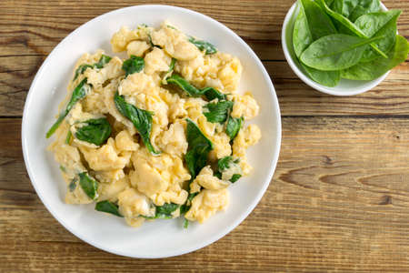scrambled eggs with spinach in a white plate. on a wooden tableの写真素材