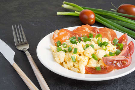 scrambled eggs with tomatoes on a white plate. on a wooden tableの写真素材