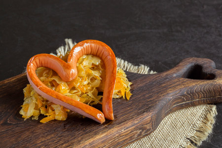 braised pickled cabbage with grilled sausage in the shape of a heart. on a wooden boardの写真素材