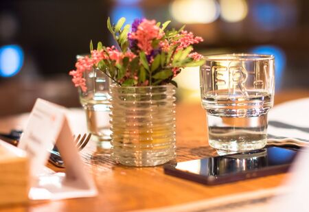 The glass of water and a glass with a pink lilac on the table next to a mobile phone. Shallow depth...