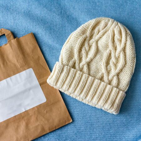 White hat knitted by hand from wool on a blue background next to a natural paper bagの写真素材