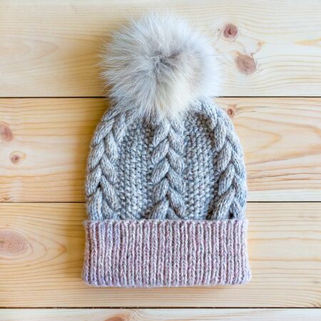 manually knitted on needles the hat is gray with a pink pompom on a natural wooden background