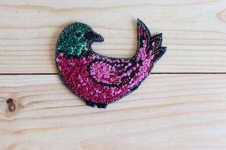 brooch embroidered with beads in the shape of a bird on a wooden backgroundの写真素材