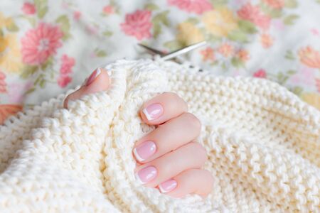 Little female hand with manicure holds connected to the spokes of a soft beige sweater yarn. Focus on the big toe.の写真素材