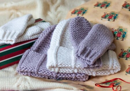 Hats and mittens out of focus next to the gift box and wrapping paper