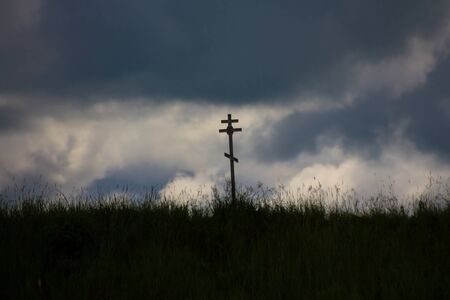 Orthodox cross in high green grass on a background gloomy skyの写真素材