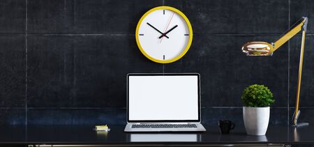laptop on desk with plant, desk lamp, yellow wall watch and black concrete wall 3D renderingの写真素材