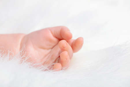 Hand of a sleeping baby, lying on white fur.