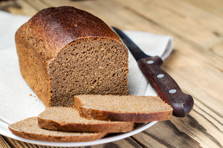 A loaf of sliced ??brown bread in a bowl on a wooden table. Shallow DOF