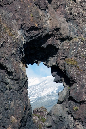 The west of Iceland, at the western end of the peninsula Sneifellsnes, in the lava field of Hellnar, hole in the lava overlooking the snow-covered slope of Sneifellsjoekullの写真素材