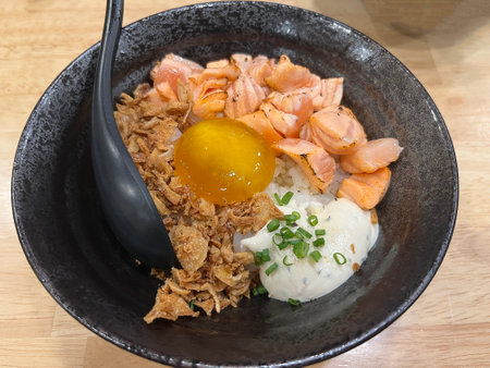 Rice topped with smoked salmon and egg yolk in black bowlの写真素材