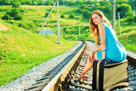 pretty girl sitting on a suitcase on the train tracksの写真素材