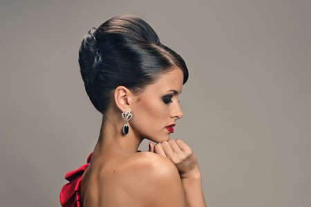 portrait of beautiful girl with elegant coiffure and red dress on grey