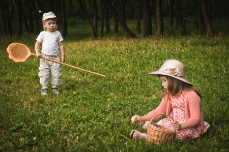 little boy with butterfly net and girl on the grass in the forest, focus on the boyの写真素材