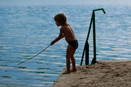 Boy fishes on the bank of small river. branch instead hookの写真素材