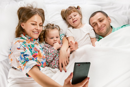 Happy young family taking selfies with her smartphone in the bed, Above viewの写真素材
