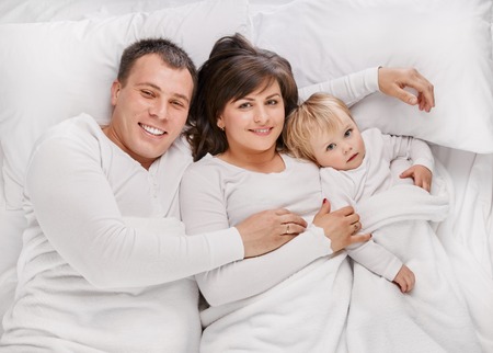 Above view of a family lying on the bed, parents playing with their little daughterの写真素材