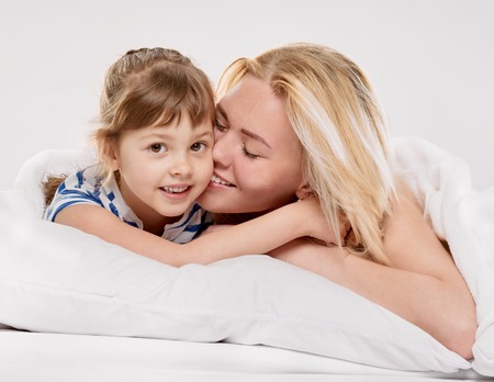 Portrait of a joyful mother and her little daughter in the bed on light grey backgroundの写真素材