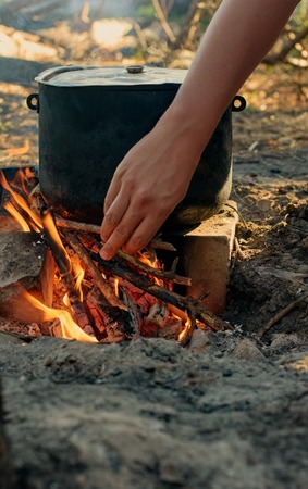 Tourist kettle on camp fire. hand with firewoodの写真素材
